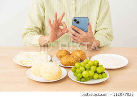 一名中年婦女拿著含有大量糖(碳水化合物)的食物和智慧型手機,並做了一個圓圈標誌 一名中年婦女拿著含有大量糖(碳水化合物)的食物和智慧型手機,並做了一個圓圈標誌 112077022