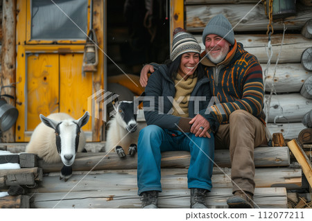 Happy couple sitting on the steps with goats near the house 112077211