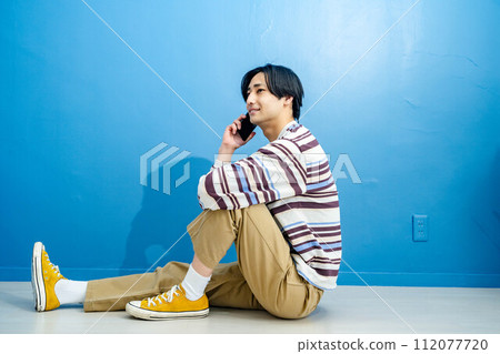 Young man making a phone call on blue background Young man making a phone call on blue background 112077720