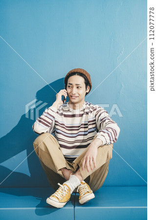 一個戴著帽子、在藍色背景下操作智慧型手機的年輕人 一個戴著帽子、在藍色背景下操作智慧型手機的年輕人 112077778