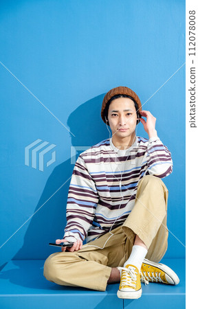 藍色背景下,戴著眼鏡和帽子玩智慧型手機的年輕人 藍色背景下,戴著眼鏡和帽子玩智慧型手機的年輕人 112078008