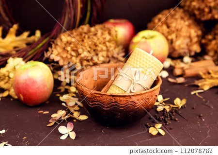 beeswax candle, bowl, apple and dry hydrangea flowers on brown background. Honey autumn cozy aroma candle for interior and tradition. Mockup, autumn composition, still life 112078782