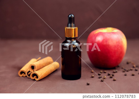 essential oil in brown glass bottle with pipette, cosmetology serum product for moisturizer facial care, apple and cinnamon sticks on brown background. Cosmetic skincare product blank package, mockup essential oil in brown glass bottle with pipette, cosmetology serum product for moisturizer facial care, apple and cinnamon sticks on brown background. Cosmetic skincare product blank package, mockup 112078783
