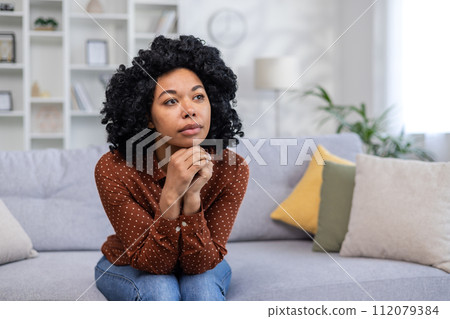 Sad and pensive African American woman sitting sullen at home and suffering from depression, crying after receiving bad news. Sad and pensive African American woman sitting sullen at home and suffering from depression, crying after receiving bad news. 112079384