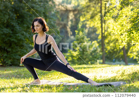 A calm woman in a yoga pose outdoors, highlighted by the warm sunset. A serene moment capturing health and wellness. A calm woman in a yoga pose outdoors, highlighted by the warm sunset. A serene moment capturing health and wellness. 112079440