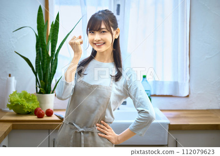 Smiling young housewife wearing an apron posing in the kitchen 112079623