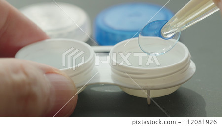 Close-up of contact lens container with tweezers in hand retrieving a lens 112081926