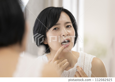 A woman in her early 50s worries about her gums while brushing her teeth. A woman in her early 50s worries about her gums while brushing her teeth. 112082925