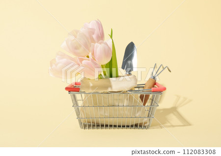 Garden tools, flowers in bag and shopping basket on light background Garden tools, flowers in bag and shopping basket on light background 112083308