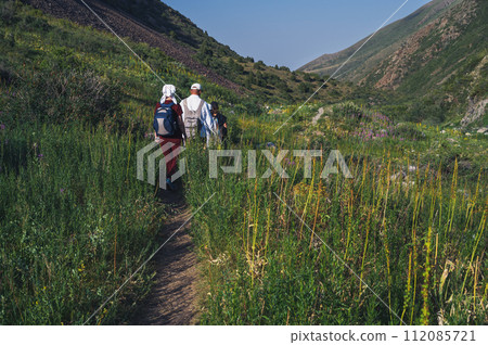 group of tourists travelers with backpacks hiking in field in valley in mountains in summer group of tourists travelers with backpacks hiking in field in valley in mountains in summer 112085721