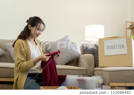 Woman asian holding donation box full with clothes and select clothes. Concept of donation and clothes recycling. Helping poor people 112086482