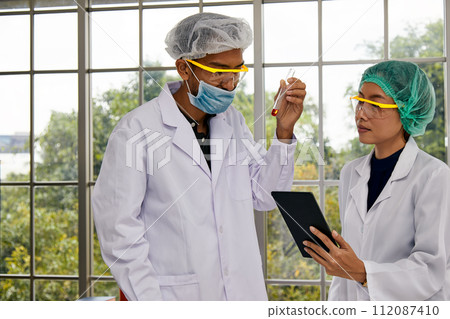 Two Scientists Combine Efforts with Test Tube and Tablet Analysis; Teamwork in Scientific Research 112087410