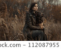 Pretty woman dressed in a brown fur jacket, hugs her dog in the field 112087955
