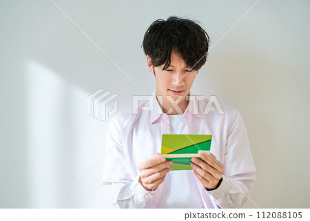 Young man looking at his bankbook and feeling disappointed Young man looking at his bankbook and feeling disappointed 112088105