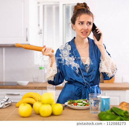 Portrait of housewife with rolling pin talking on phone Portrait of housewife with rolling pin talking on phone 112088273
