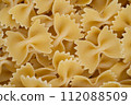 A background filled with uncooked farfalle pasta, presenting the bow-tie shape and texture characteristic of this Italian food. 112088509
