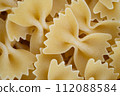 Close-up image showcasing the detailed texture of uncooked farfalle pasta, with a monochromatic yellow theme for culinary appeal. 112088584
