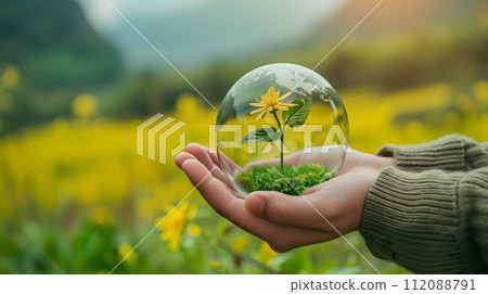 A hand cradles a transparent globe encapsulating a single blooming flower, symbolizing environmental care and protection. 112088791
