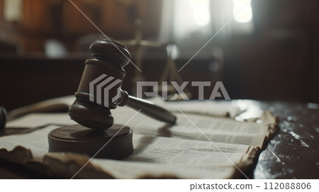 The image depicts a wooden gavel resting on an open legal book, symbolizing law, authority, and justice in a courtroom atmosphere. 112088806