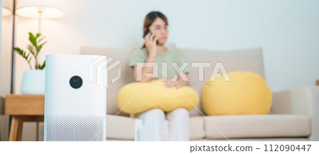 Air Purifier with woman relax and use smartphone on sofa. Purification system for filter and cleaning dust PM2.5 HEPA and virus in home. Allergy, Pure air, health, Wellness lifestyle and Air Pollution Air Purifier with woman relax and use smartphone on sofa. Purification system for filter and cleaning dust PM2.5 HEPA and virus in home. Allergy, Pure air, health, Wellness lifestyle and Air Pollution 112090447
