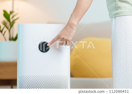Woman turn on Air Purifier in living room. Purification system for filter and cleaning dust PM2.5 HEPA and virus in home. Allergy, Pure air, health lifestyle, Wellness life and Air Pollution 112090451