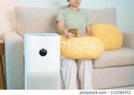 Air Purifier with woman relax and use smartphone on sofa. Purification system for filter and cleaning dust PM2.5 HEPA and virus in home. Allergy, Pure air, health, Wellness lifestyle and Air Pollution Air Purifier with woman relax and use smartphone on sofa. Purification system for filter and cleaning dust PM2.5 HEPA and virus in home. Allergy, Pure air, health, Wellness lifestyle and Air Pollution 112090452