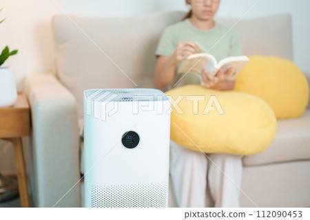 Air Purifier with woman read and relax on sofa. Purification system for filter and cleaning dust PM2.5 HEPA and virus in home. Allergy, Pure air, health lifestyle, Wellness life and Air Pollution 112090453