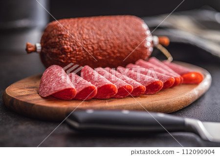 Sliced smoked salami sausages on cutting board on black table. Sliced smoked salami sausages on cutting board on black table. 112090904