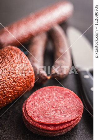 Sliced smoked salami sausages on black table. 112090938