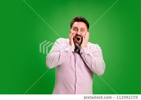 Pleasant surprised man put hands on face with wow facial-expression against vibrant green studio background. Positive emotions. Pleasant surprised man put hands on face with wow facial-expression against vibrant green studio background. Positive emotions. 112092259