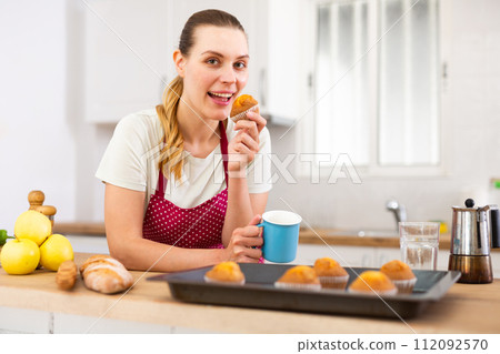 Smiling young woman in apron eating cupcakes from baking tray Smiling young woman in apron eating cupcakes from baking tray 112092570