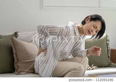 A woman in her early 50s with a painful expression, putting her hands on her hips 112093296