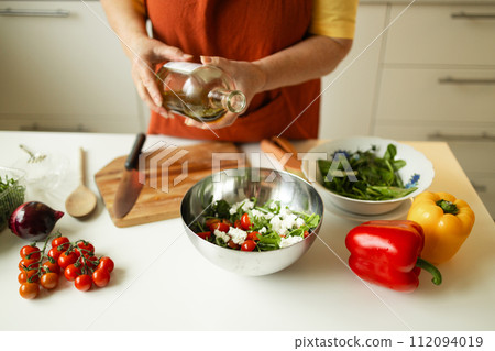 Female chef in a uniform pours olive oil from a bottle. Caucasian female food blogger working explaining how to cook a dish 112094019