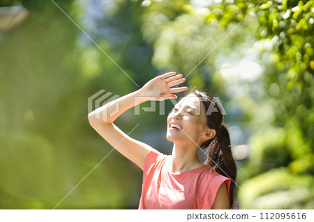 Young woman in sportswear wiping sweat with towel in greenery Young woman in sportswear wiping sweat with towel in greenery 112095616