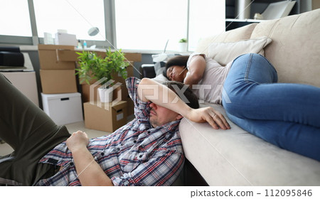 Young homeowners resting on couch and floor Young homeowners resting on couch and floor 112095846