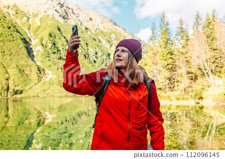 Lost trekker traveler 30s woman searching location with smart phone alone in a forest near Morskie Oko. Hiker female has lost the cellular signal and lift up the smartphone to improve the quality of 112096145