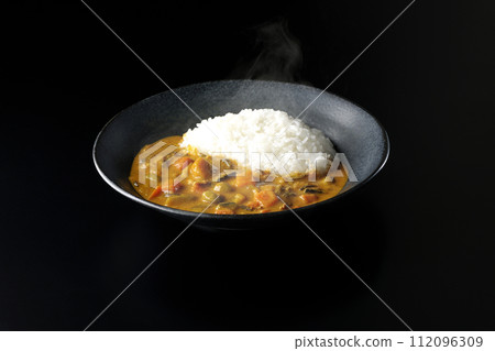 一張黑色背景下熱騰騰的咖哩飯和大量豬肉、南瓜和胡蘿蔔等蔬菜的照片。 一張黑色背景下熱騰騰的咖哩飯和大量豬肉、南瓜和胡蘿蔔等蔬菜的照片。 112096309
