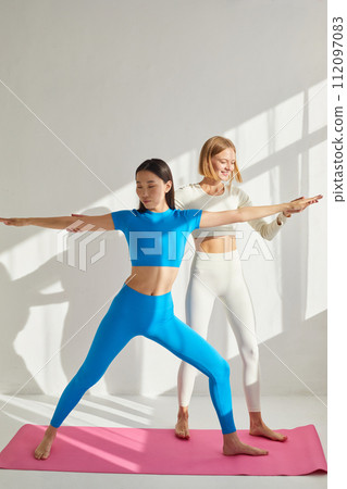 Yoga coach woman is teaching asian woman yoga and stretching. Concept of physical and mental health care, asian and caucasian ethnicity 112097083