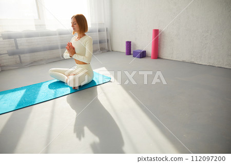 Woman practicing yoga and meditation in lotus pose on yoga mat, relaxed with closed eyes. Mindful meditation concept. 112097200