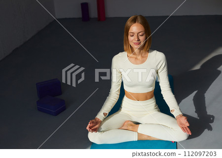 Woman practicing yoga and meditation in lotus pose on yoga mat, relaxed with closed eyes. Mindful meditation concept. 112097203