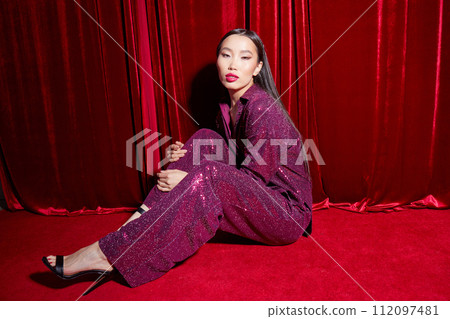 Fashion asian female model in burgundy glitter suit, on red fabric background. Fashion asian female model in burgundy glitter suit, on red fabric background. 112097481
