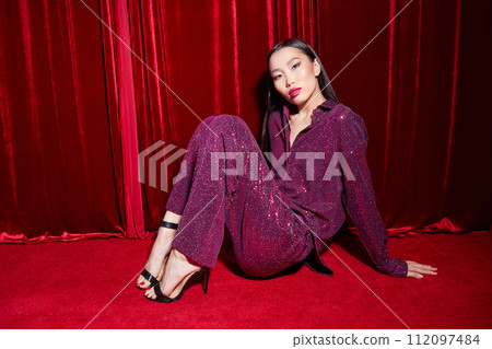 Fashion asian female model in burgundy glitter suit, on red fabric background. Fashion asian female model in burgundy glitter suit, on red fabric background. 112097484