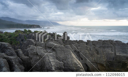 Sunset over rough ocean coast with big waves and pancake like rocks in foreground, New Zealand Sunset over rough ocean coast with big waves and pancake like rocks in foreground, New Zealand 112098015