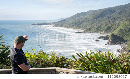 Man enjoying view on rough exotic coastal landscape during sunny day, New Zealand Man enjoying view on rough exotic coastal landscape during sunny day, New Zealand 112098017