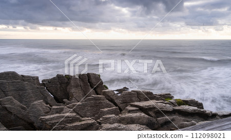 Sunset over rough ocean coast with waves and pancake like rocks in foreground, New Zealand Sunset over rough ocean coast with waves and pancake like rocks in foreground, New Zealand 112098021