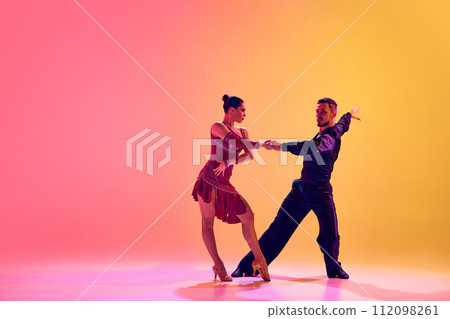 Elegant young woman and handsome man, ballroom dancers in motion, dancing against gradient pink yellow background in neon light Elegant young woman and handsome man, ballroom dancers in motion, dancing against gradient pink yellow background in neon light 112098261