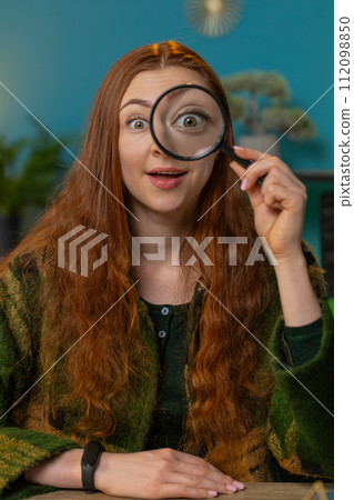 Amazed woman holds magnifying glass near face looking at camera with big zoomed eye analyzing wow Amazed woman holds magnifying glass near face looking at camera with big zoomed eye analyzing wow 112098850