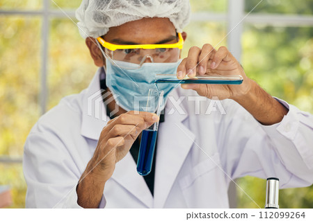 Asian male Chemist Conducting Performing Liquid Experiment with Test Tubes 112099264