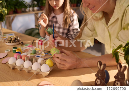 Selective focus shot of mother and daughter sitting at wooden desk in workshop coloring eggs for Easter Selective focus shot of mother and daughter sitting at wooden desk in workshop coloring eggs for Easter 112099700
