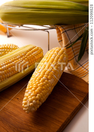 Clous up view of cutting board with three cobs sweet corn on white wooden background.. Clous up view of cutting board with three cobs sweet corn on white wooden background.. 112099828